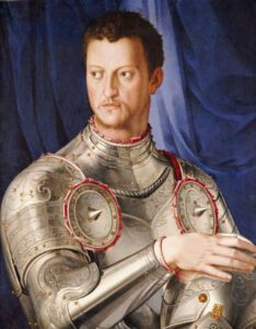 Portrait of young Duke Cosimo I de Medici. He barely has any beard, and looks barely twenty. He wears very elaborately dec orated etched shiny armor, with a helmet in his hands, and stands in front of a velvety drape. He has no insignia of knighthood etc. but looks very warlike, and his armor has brackets for bracing a lance, for jousting.