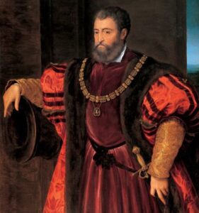 Portrait of Duke Alfonso d'Este. He has a grizzled full beard. Wearing a red and black fur - lined brocade overgarment over a red velvet robe, he leans nonchalantly on a cannon, with his other hand on the gold - hilted sword at his b elt. A dignified chain of membership in a prestigious order of knighthood hangs around his neck (Order of Saint Michael, of France).